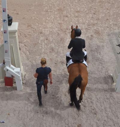 groom walking rider and horse into the arena from above