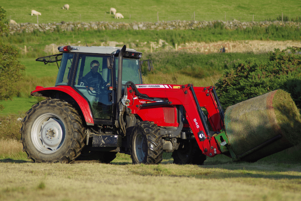 red tractor transporting a round bale of hay